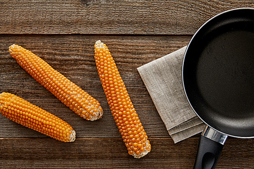 top view of delicious corn near frying pan on wooden background
