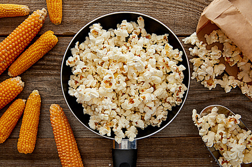 top view of popcorn in frying pan near ripe corn on wooden background