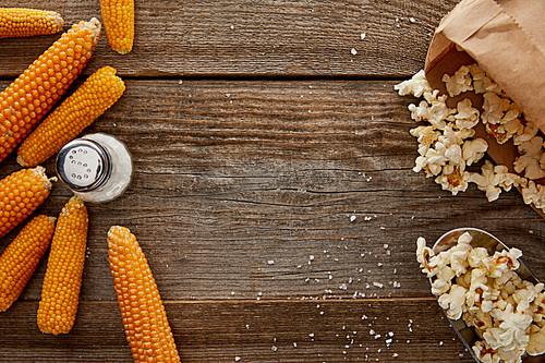 top view of delicious popcorn and corn with salt on wooden background