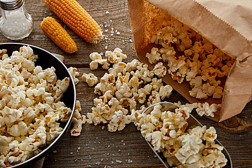 delicious popcorn in frying pan near corn and salt on wooden background