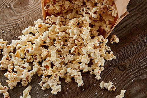 delicious crispy popcorn scattered from paper bag on wooden background