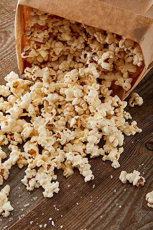 tasty popcorn scattered from paper bag on wooden background