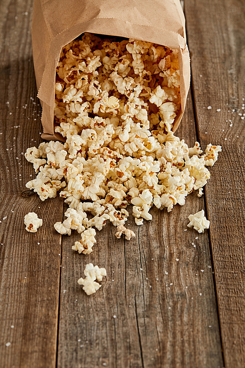 delicious popcorn scattered from paper bag on wooden background with copy space