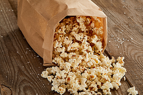 delicious popcorn scattered from paper bag on wooden background