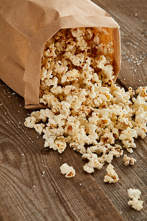 salty delicious popcorn scattered from paper bag on wooden surface