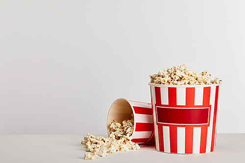 tasty popcorn scattered from red striped paper buckets isolated on grey