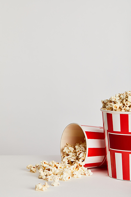 popcorn scattered from red striped paper buckets isolated on grey
