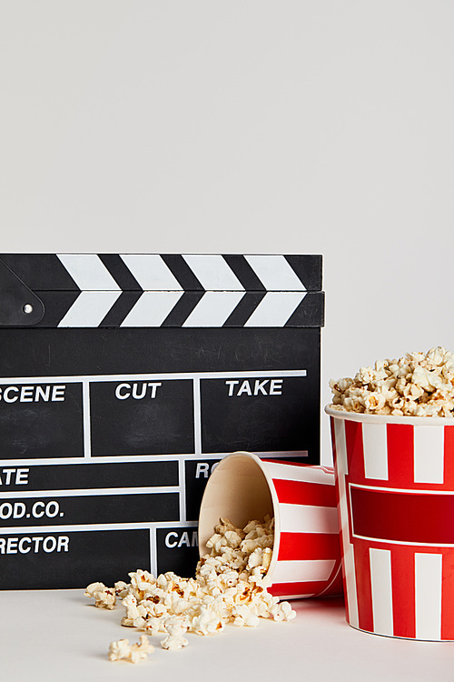 delicious popcorn in striped buckets near clapper board isolated on grey