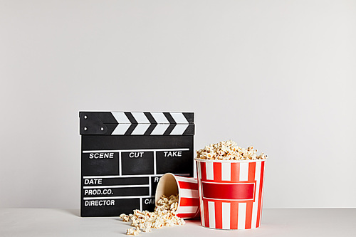 popcorn in striped buckets near clapper board isolated on grey