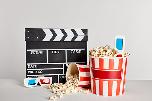 delicious popcorn scattered from buckets with clapper board and 3d glasses isolated on grey
