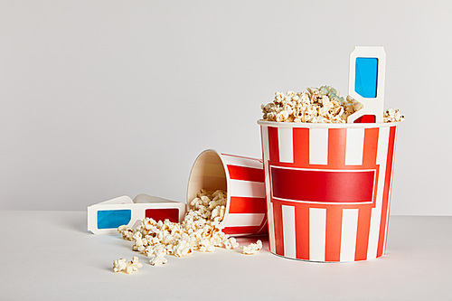 delicious popcorn in striped buckets with 3d glasses isolated on grey