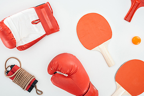 top view of boxing gloves near red ping pong rackets and skipping rope isolated on white
