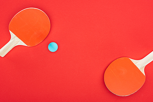 top view of blue ping pong ball near rackets isolated on red
