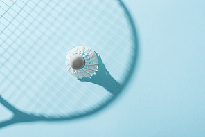 top view of white shuttlecock with feathers near shadow of badminton racket on blue