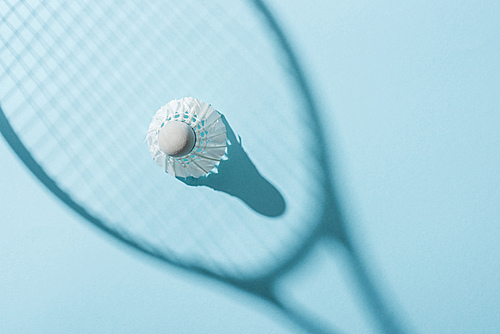 top view of shuttlecock with white feathers near shadow of badminton racket on blue