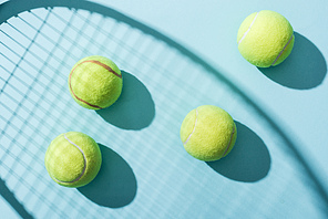 top view of tennis balls near shadow of tennis racket on blue
