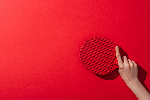 cropped view of woman holding wooden table tennis racket on red