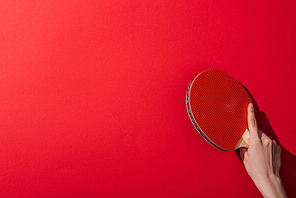 cropped view of woman holding table tennis racket on red