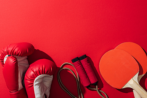 top view of boxing gloves near red ping pong rackets and skipping rope on red