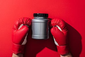 cropped view of boxer holding grey jar in boxing gloves on red