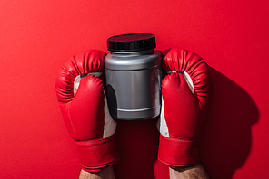 cropped view of man holding grey jar in boxing gloves on red
