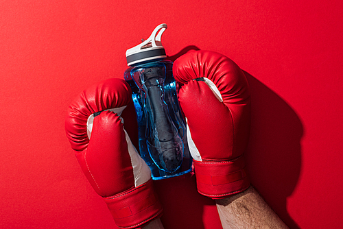 cropped view of boxer holding sport bottle with boxing gloves on red