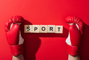 cropped view of man in boxing gloves near wooden cubes with sport lettering on red