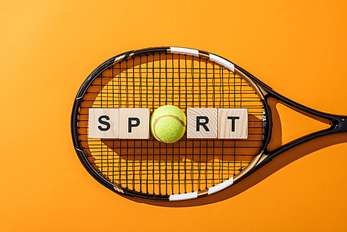 top view of wooden cubes with sport lettering near tennis ball and tennis racket on yellow