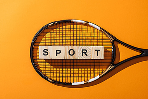 top view of wooden cubes with sport lettering near tennis racket on yellow