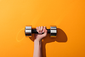 cropped view of woman holding heavy dumbbell while exercising on yellow