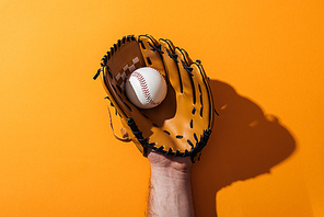 cropped view of man holding softball in brown baseball glove on yellow