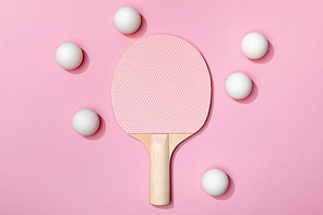 top view of white table tennis balls near wooden pink racket on pink background