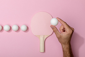 cropped view of man holding white table tennis ball near racket on pink background