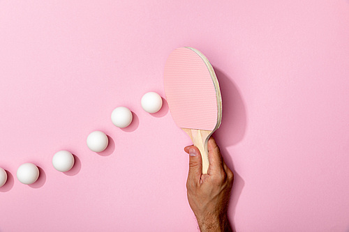 cropped view of man holding table tennis racket near white balls on pink background