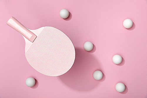 top view of white table tennis balls scattered under racket on pink background