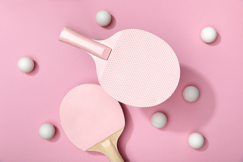 top view of white table tennis balls and rackets on pink background