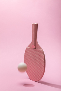 ping-pong racket and white flying ball on pink background with copy space