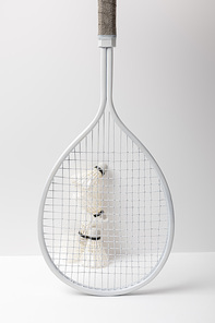 white badminton shuttlecocks behind white racket on white background