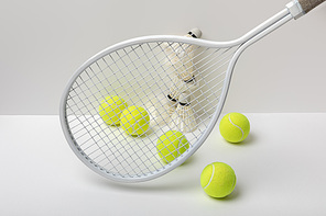 white badminton shuttlecocks and bright yellow tennis balls near racket on white background