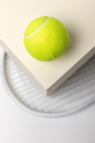 selective focus of bright yellow tennis ball on cube and racket on white background