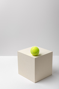 bright yellow tennis ball on square cube on white background