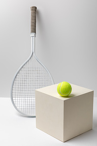 tennis racket and bright yellow tennis ball on cube on white background