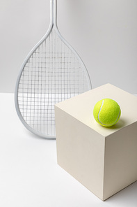 bright yellow tennis ball on cube near racket on white background