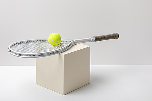 yellow tennis ball with racket on cube on white background