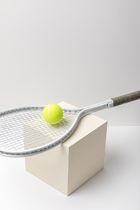 bright yellow tennis ball with racket on cube on white background