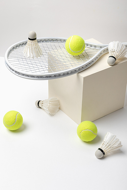 tennis racket and bright yellow tennis balls with shuttlecocks on cube on white background