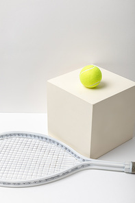 tennis racket and bright yellow tennis ball on cube on white background