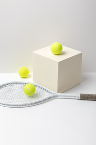 tennis racket and bright yellow tennis balls on cube on white background