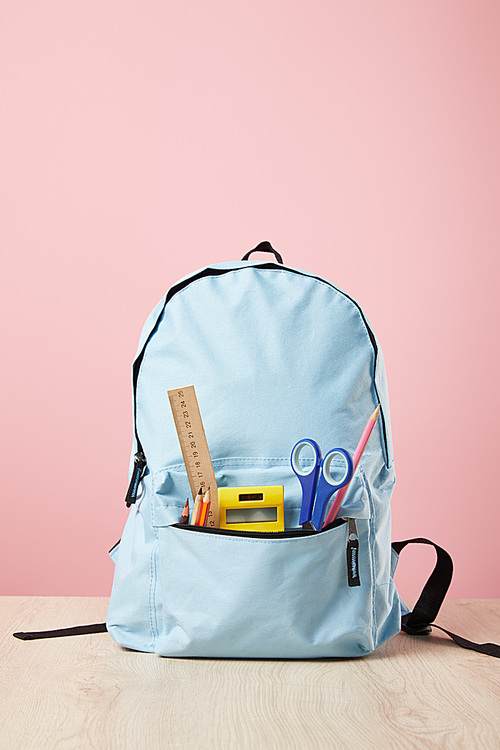 school blue backpack with supplies in pocket isolated on pink