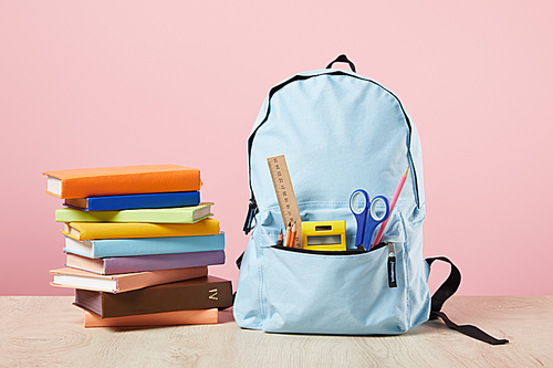 school blue backpack with supplies in pocket near books isolated on pink